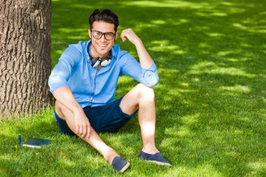 gülümseyen adam parkta çim üzerinde bir kitap tutan