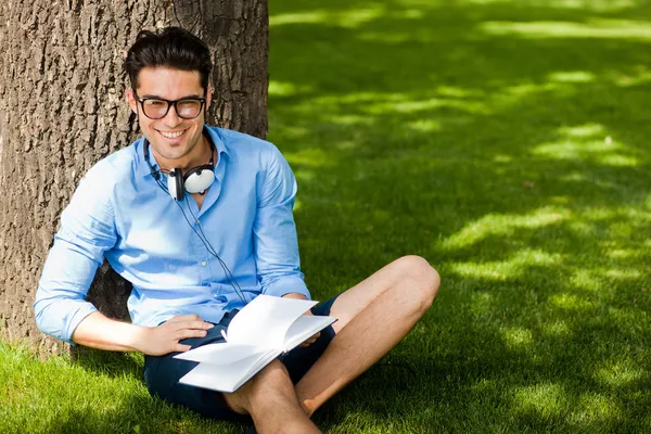 Gülümseyen adam parkta çim üzerinde bir kitap tutan — Stok fotoğraf