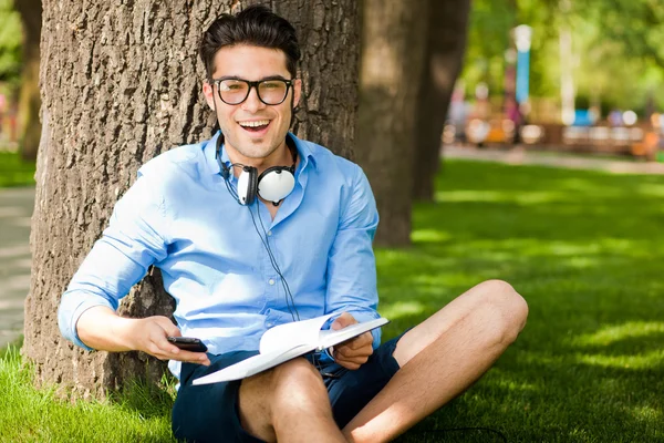 Sorrindo homem segurando um livro na grama no parque — Fotografia de Stock