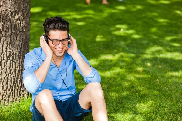 Homem bonito sorrindo e ouvindo música na grama no — Fotografia de Stock