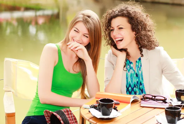 Zwei schöne Frauen lachen über einen Kaffee auf der Flussterrasse Stockbild