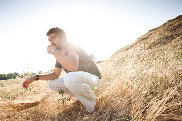 Man on dry meadow picking grass straws to start a fire, wide angle view - into the wild series — Stock Photo, Image