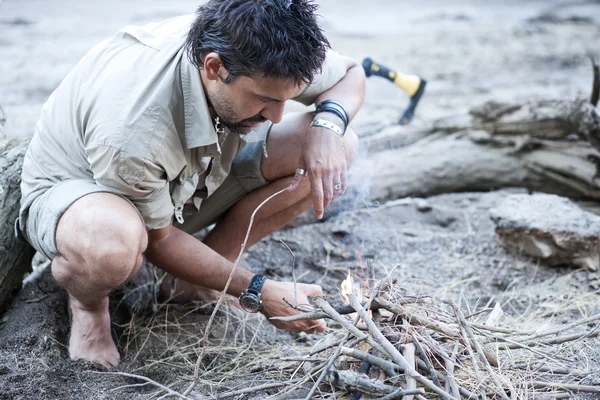 Man preparing a fire on the beach by the river — Stock Photo, Image