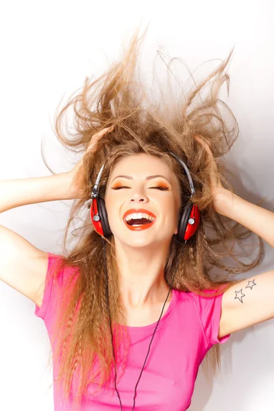 Χαριτωμένο σγουρό ξανθό κορίτσι που ακούτε μουσική στο μεγάλο κόκκινο ακουστικά που απομονώνονται σε λευκό — Φωτογραφία Αρχείου