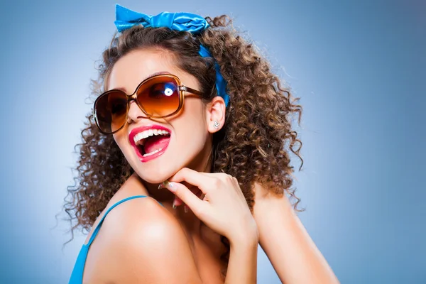 Nettes Pin-up-Mädchen mit lockigem Haar und perfekten Zähnen auf blauem Hintergrund Stockbild