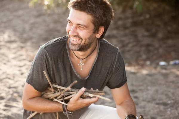 Uomo ruvido raccogliere legna per fare fuoco vicino al fiume - nella serie selvaggia Fotografia Stock