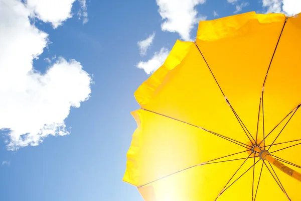 Gelber Regenschirm am blauen Himmel mit Wolken Stockbild