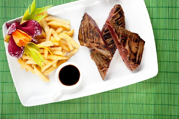 Delicious steak with french fries and souce on dish, bambus back — Stock Photo, Image