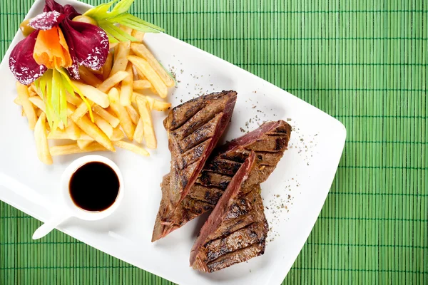 Delicious steak with french fries and souce on dish, bambus back — Stock Photo, Image