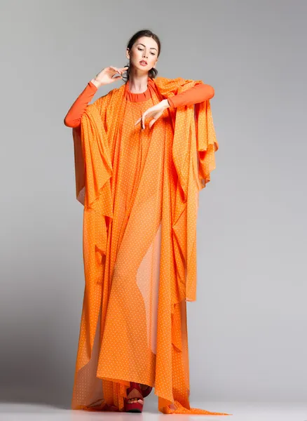 Schöne Frau in langem orangefarbenem Kleid posiert dynamisch im Studio — Stockfoto