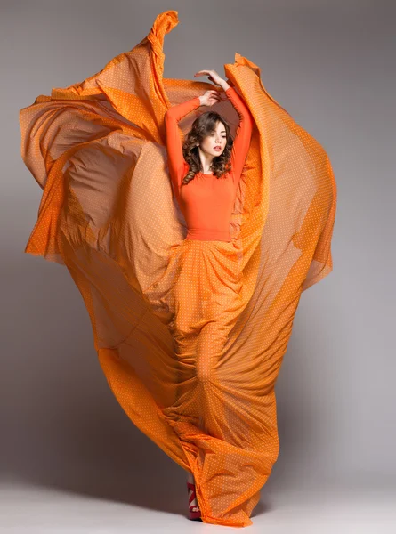 Bela mulher em vestido laranja longo posando dinâmica no estúdio — Fotografia de Stock