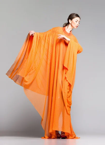 Bela mulher em vestido laranja longo posando dinâmica no estúdio — Fotografia de Stock