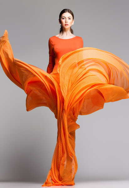 beautiful woman in long orange dress posing dynamic in the studio