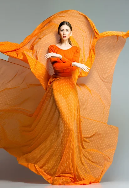 Schöne Frau in langem orangefarbenem Kleid posiert dynamisch im Studio — Stockfoto