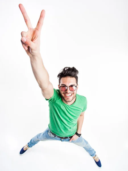 Gracioso hombre guapo con gafas hipster mostrando la victoria y sonriendo - tiro de gran angular — Foto de Stock