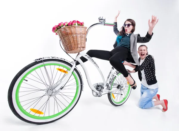 Dos chicas montando en bicicleta haciendo caras graciosas - aisladas sobre fondo azulado — Foto de Stock