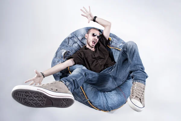 Funny crazy man dressed in jeans and sneakers standing on denim beanbag — Stock Photo, Image