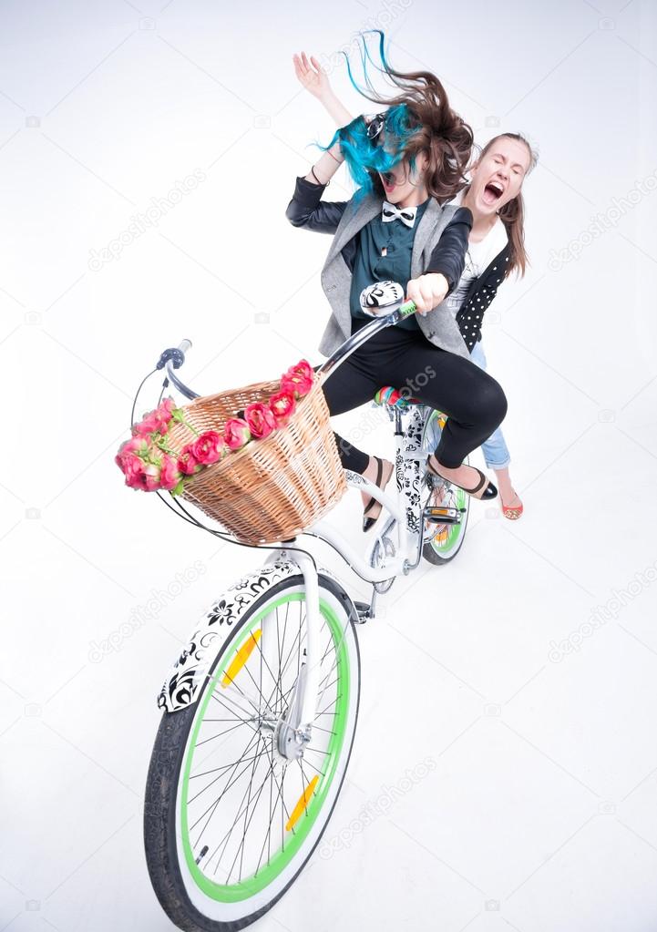 two girls riding a bike making funny faces - isolated on bluish background