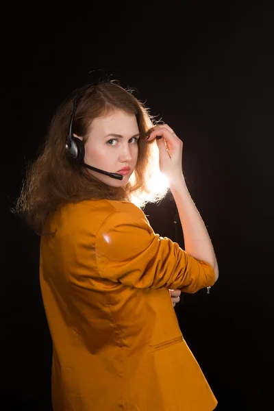 Young beautiful woman-operator with headphone smiles, it is isolated on black background. — Stock Photo, Image