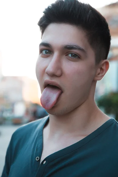 Attraktiver junger Mann zeigt seine Zunge im urbanen Hintergrund — Stockfoto
