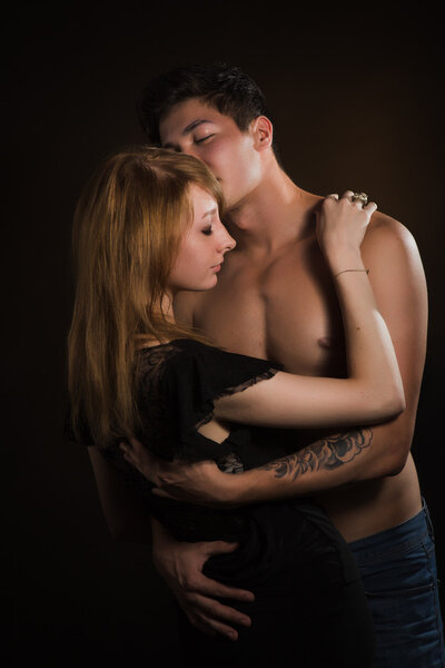 Beautiful young couple hugging and kissing isolated on black background.