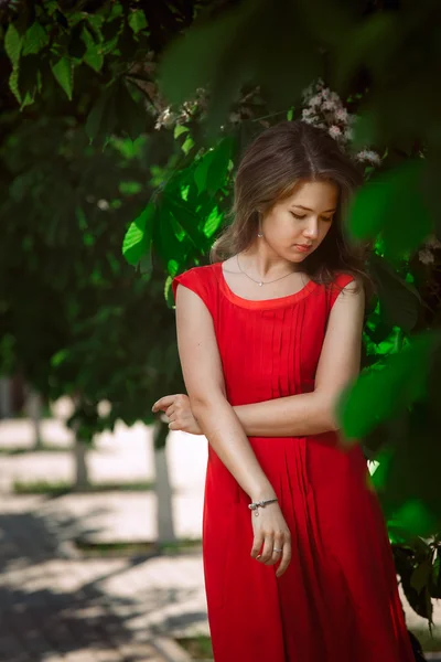 Portrait of a beautiful sexy fashion girl in a red dress on the nature of the park, with dark hair and a leather belt — Stock Photo, Image
