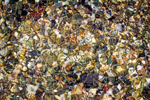 Pequeñas piedras marinas en la orilla del mar, cubiertas por una ola marina . —  Fotos de Stock