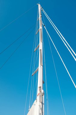 Katı mavi bir arka planda yelkenli bir gemide beyaz büyük direkler.