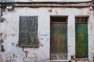Terk edilmiş bina cephesi, hasarlı duvar, kapalı ahşap kapılar ve pencereler.