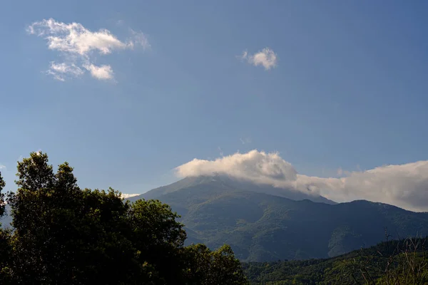 緑豊かな自然の中で青い空に山の頂上を覆う白い雲日当たりの良い風景 — ストック写真