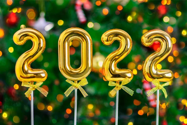 Altın figürler 2022 noel ağacının bulanık arka planında çelenk ve bokeh ışıklarıyla. Yılbaşı tebrik kartı, etkinlik ve parti için şablon.