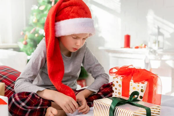 Pijamalı, kırmızı şapkalı, üzgün bir çocuk yatakta oturup Noel Baba 'nın hediye kutularına sinirli bir şekilde bakıyor. Çocuk yeni yıl hediyesiyle hayal kırıklığına uğradı..