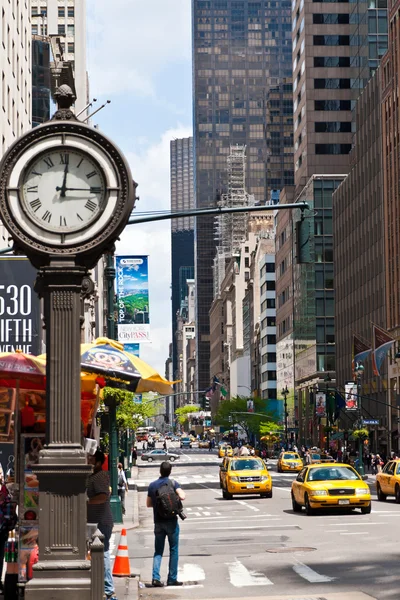 Vida urbana da cidade de Nova York com táxis passando pela 5th avenue e um grande relógio de rua . — Fotografia de Stock