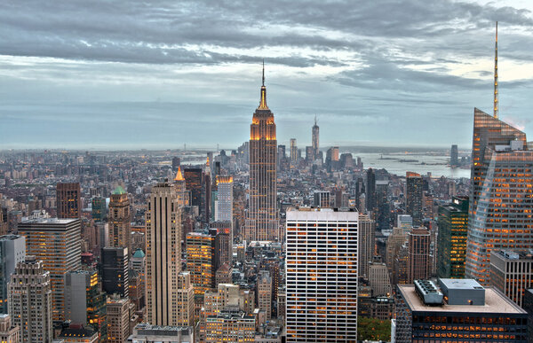 Empire State and Manhattan buildings with lights on from a high view, in the dusk of New York City, USA.
