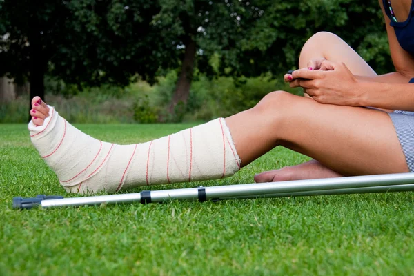 Girl with leg in plaster chatting with her smartphone — Stock Photo, Image