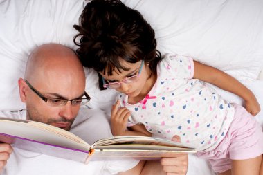 Baba ve kızı yatakta kitap okuyor.
