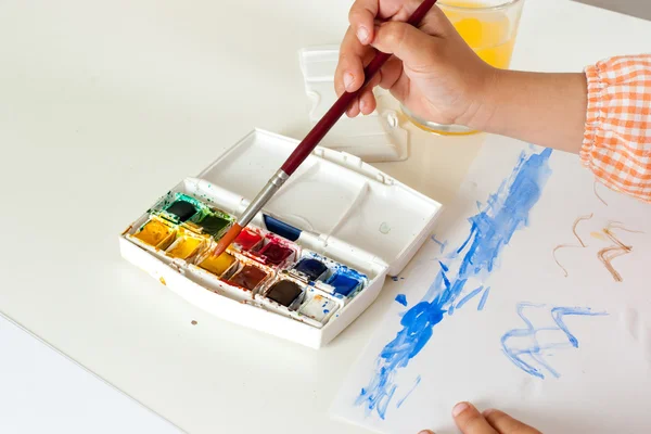 Hand of child with paintbrush on watercolor set — Stock Photo, Image