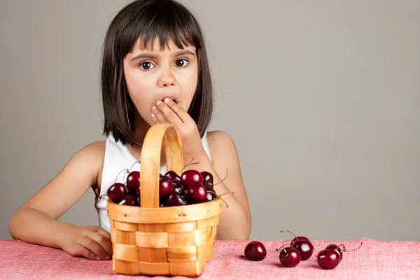 Vacker liten flicka äter körsbär från en korg — Stockfoto