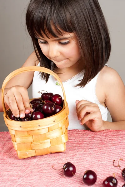 Lilla flickan att välja körsbär från en korg — Stockfoto