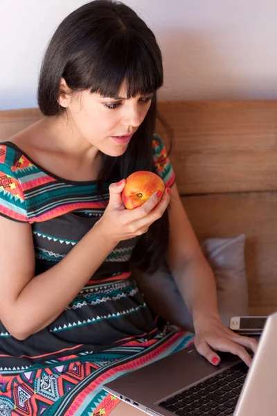 Mujer joven tomando un aperitivo saludable mientras trabaja —  Fotos de Stock