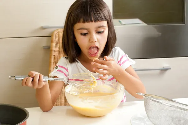 Glückliches kleines Mädchen, das die Mischung probiert, um einen Kuchen zu kochen — Stockfoto