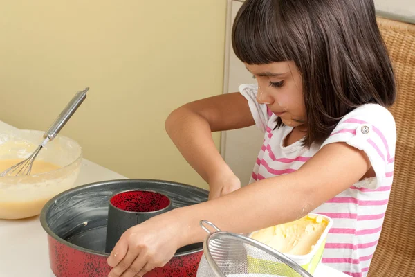 Glückliches kleines Mädchen schmiert eine Form, um einen Kuchen zu backen — Stockfoto