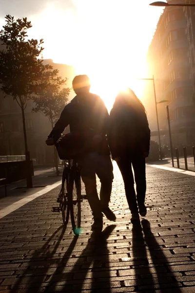 Pareja joven caminando por la calle con una bicicleta al atardecer . — Foto de Stock