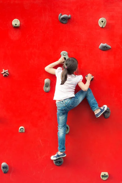 Chica escalando una pared roja en un patio de recreo —  Fotos de Stock