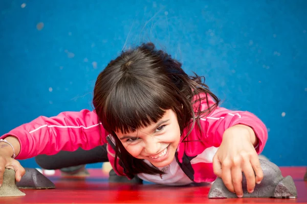 Красива дівчина піднімається на червону стіну на дитячому майданчику — стокове фото