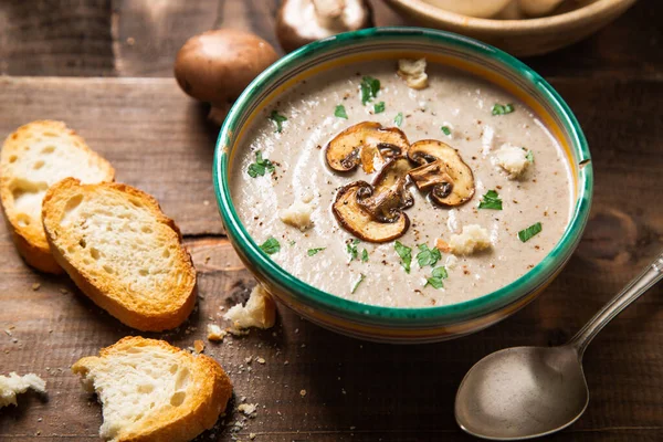 Homemade creamy mushroom soup with sliced mushrooms topping in an old bowl and bread toast on a rustic wooden table