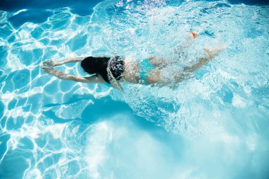 Turkuaz bikinili genç bir kadının yazın yüzme havuzunda suyun altında yüzüşünün en güzel görüntüsü.