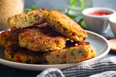Domates ve yoğurt sosuyla servis edilen glütensiz vejetaryen darı ve sebze burgeri.