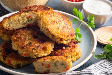 Domates ve yoğurt sosuyla servis edilen glütensiz vejetaryen darı ve sebze burgeri.