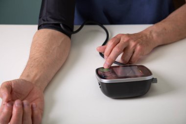 Middle aged man testing his blood pressure at home with a digital blood pressure monitor
